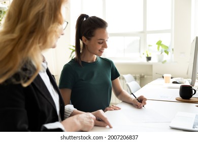 Mature business teacher supervising happy student writing notes. Middle aged mentor training intern at office workplace. HR manager helping new employee to fill and sign employment agreement