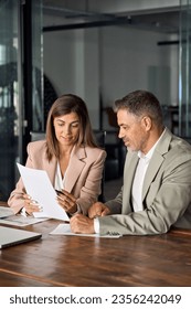 Mature business woman manager holding legal documents consulting client at office meeting, two professional executives experts discussing financial accounting papers working together. Vertical.