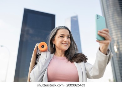 Mature Business Woman With Skateboard And Smartphone Taking Photos In The City