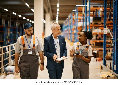 Mature businessman communicating with young workers while walking through distribution warehouse.