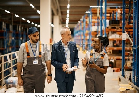 Mature businessman communicating with young workers while walking through distribution warehouse.