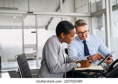 Mature businessman discussing work with black manager. Confident business man working with african american woman showing data on digital tablet. Smiling professional business people working together. - Powered by Shutterstock