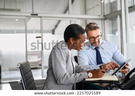 Mature businessman discussing work with black manager. Confident business man working with african american woman showing data on digital tablet. Smiling professional business people working together.