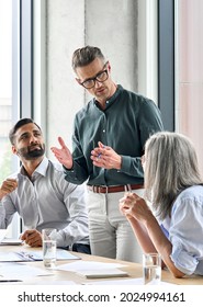 Mature businessman leader mentor talking to diverse colleagues team listening to caucasian ceo. Multicultural professionals project managers group negotiating in boardroom at meeting. Vertical. - Shutterstock ID 2024994161