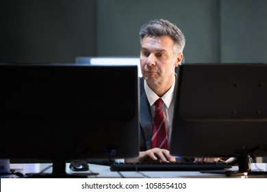 Mature Businessman Multiple Computers At Office Desk