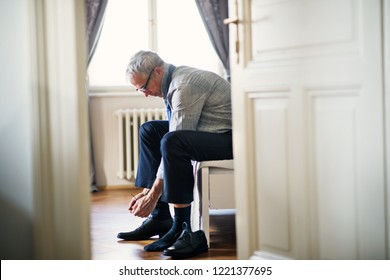 Mature businessman on a business trip sitting in a hotel room, tying shoelaces. - Powered by Shutterstock