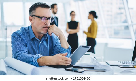 Mature Businessman In Optical Eyewear Reading Financial Publication Browsed On Modern Touch Pad Using Office Internet Connection At Table Desktop, Caucasian Executive Manager Checking Email Text