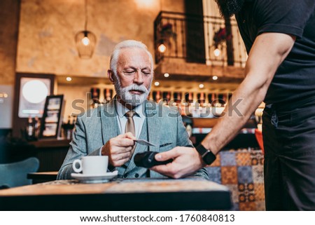 Mature businessman paying with contactless credit card with NFC technology.
