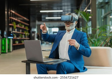 Mature businessman programmer software developer using headset app making a presentation. Watching virtual reality 3D 360 video. Bearded gray-haired guy in suit in VR goggles working at office lobby. - Powered by Shutterstock