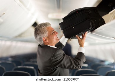 Mature Businessman Putting Luggage Into Overhead Locker On Airplane