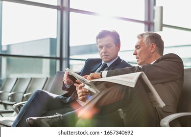 Mature businessman reading news paper while the other businessman is talking on smartphone in airport - Powered by Shutterstock - Get 15% off with code: PIKWIZARD15