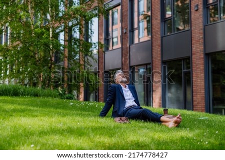 Mature businessman resting and sitting barefoot in park, feeling free, escaping from work, work life balance concept.