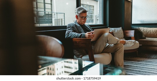 Mature businessman sitting in office lobby with a laptop. Male executive working in office lounge.