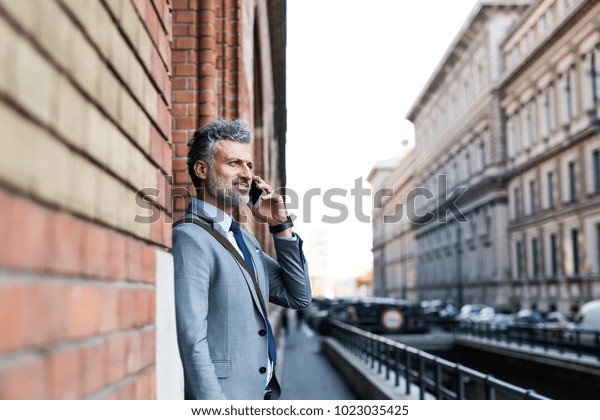 Mature businessman\
with smartphone in a\
city.