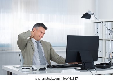 Mature Businessman Suffering From Neck Pain At Desk In Office