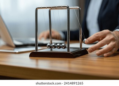 Mature businessman in a suit interacts with a Newton's cradle on his desk, symbolizing decision making and focus. - Powered by Shutterstock