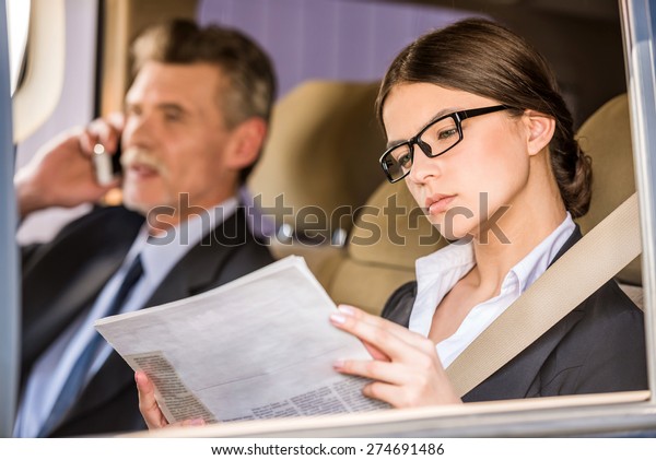 Mature businessman in\
suit sitting in the car with his beautiful personal assistant and\
talking on the phone.