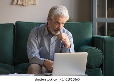 Mature Businessman Take Off Glasses Look At Pc Screen Feel Astonished Sitting On Couch At Home, Senior Man Read Shocking Online News, Worried Old Male Confused By Bad Email Or Computer Problem Concept