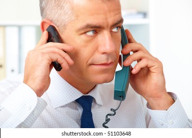 Mature Businessman With Two Phones, In The Hurry In His Office.