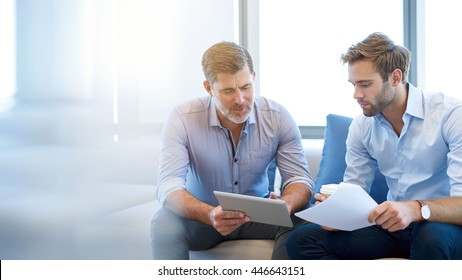 Mature businessman using a digital tablet to discuss information with a younger colleague in a modern business lounge