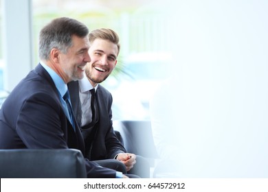 Mature businessman using a digital tablet to discuss information with a younger colleague in a modern business lounge
