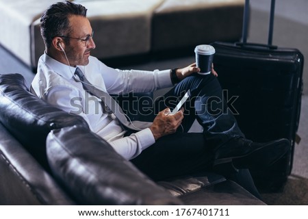 Mature businessman using a mobile phone while sitting in an airport cafe. Man waiting for his flight reading text message on his cell phone at first call lounge.