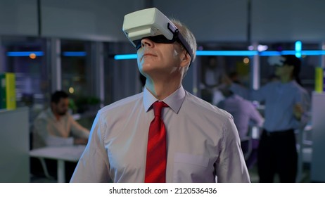 Mature businessman in virtual reality goggles in office. Male entrepreneur using vr headset working late with team - Powered by Shutterstock