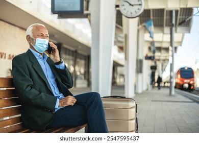 Mature businessman wearing protective face mask while talking on the phone, waiting for a train at train station. - Powered by Shutterstock