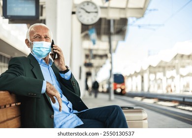 Mature businessman wearing protective face mask while talking on the phone, waiting for a train at train station. - Powered by Shutterstock