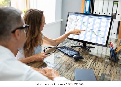 Mature Businesspeople Analyzing Gantt Chart And Calendar On Computer In Office