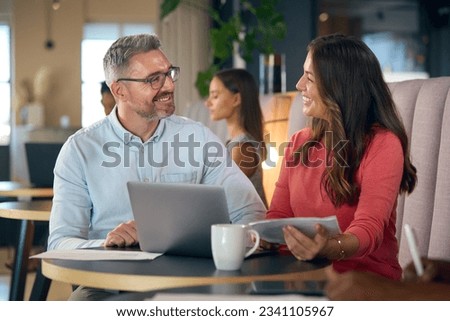 Mature Businesswoman And Businessman Working On Laptop In Informal Seating Area Of Modern Office
