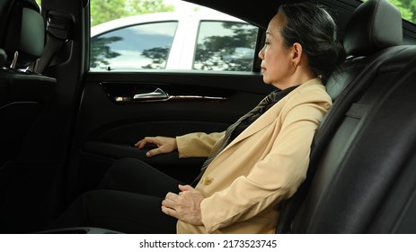 Mature Businesswoman Sitting In Car In Back Passenger Seat, Annoyed By Heavy Traffic