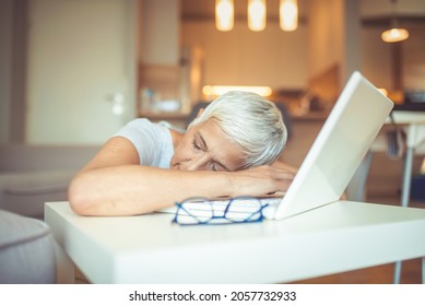 Mature Businesswoman Sleeping At Workplace. Shot Of A Mature Businesswoman Falling Asleep At Her Desk While Working In An Home Office At Night. Menopausal Mature Woman At Work Feels Bad