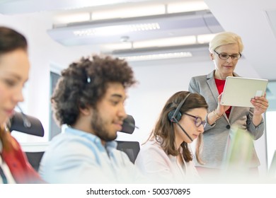 Mature businesswoman using digital tablet while operators working in office - Powered by Shutterstock