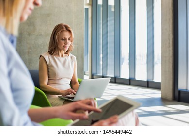 Mature businesswoman working on laptop while the other businesswoman using digital tablet sitting in lobby