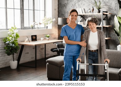 Mature caretaker nurse doctor standing with elderly senior patient grandmother using walking frame in hospice home hospital. Geriatrics concept - Shutterstock ID 2395115153