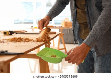 Mature carpenter sweeping filings from table in shop, closeup - Powered by Shutterstock