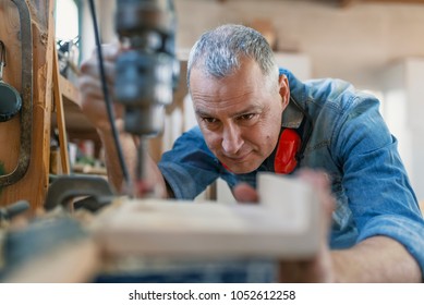 Mature Carpenter Using Drill Press In Workshop. Wood Working. Carpentry Workshop Routine. Engineer In Workshop