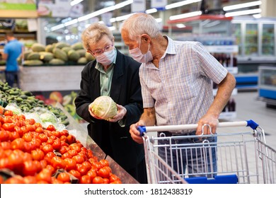 mature caucasian couple in mask and gloves with covid protection picks tomatoes in vegetable section of supermarket