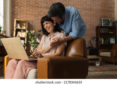 A mature Caucasian couple is using a laptop from the comfort of their home. hug smile - Powered by Shutterstock