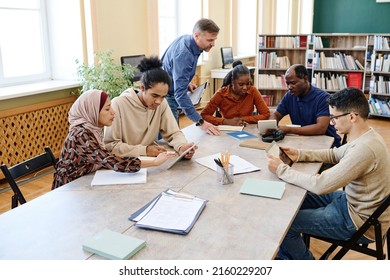 Mature Caucasian English language teacher helping immigrant students with doing task during lesson in library - Shutterstock ID 2160229207