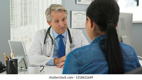 Mature Caucasian male doctor in his office listening to new patient and smiling. Primary care physician going over medical history with Japanese woman