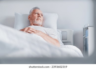 Mature caucasian male patient resting while lying on bed in modern hospital ward room. Hospitalization. Treatment and healing. Closeup image - Powered by Shutterstock