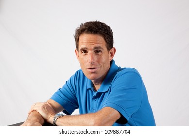 Mature Caucasian Male Sitting With His Forearms On A Table, Talking To  The Camera