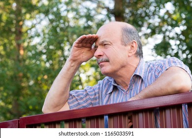 Mature caucasian man carefully watching over the fence. Concept of curious neighbors and private life