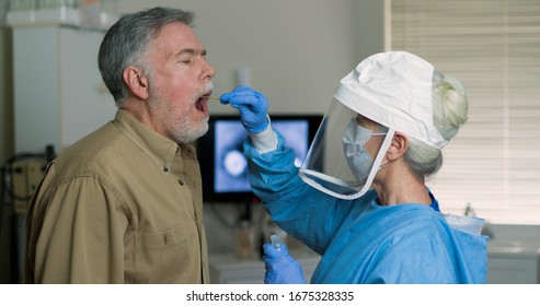 A mature Caucasian man in a clinical setting being swabbed by a healthcare worker in protective garb to determine if he has contracted the coronavirus or COVID-19.