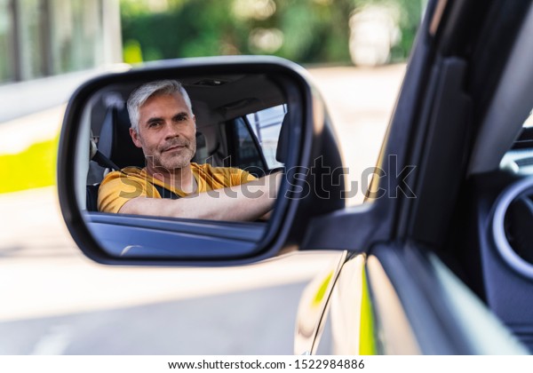 Mature Caucasian man looking at mirror of his new\
car. Travelling concept