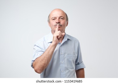 Mature caucasian man wearing blue shirt making silence gesture. Be quiet please concept