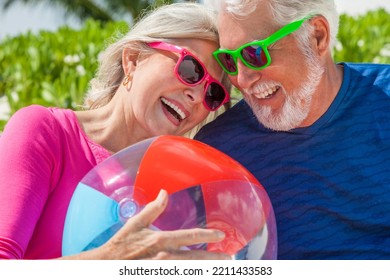 Mature Caucasian Senior Couple In Colourful Clothing Carefree Outdoors With A Beach Ball On Tropical Luxury Caribbean Resort 