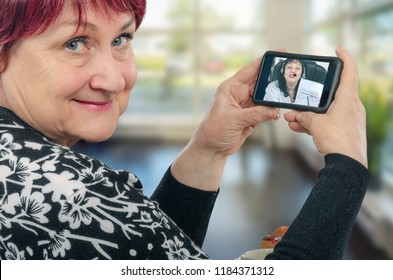 Mature Caucasian Woman Enjoys Telecommunication With Virtual Doctor. She Holds Her Mobile Phone In Two Hands The Physician Talks To Her On The Screen Showing Some Diagrams.